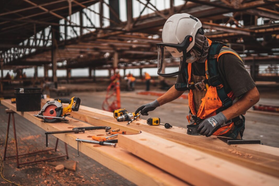 Photo by Jeriden Villegas man in orange and black vest wearing white helmet holding yellow and black power tool