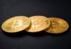 three gold-colored bitcoins on black surface