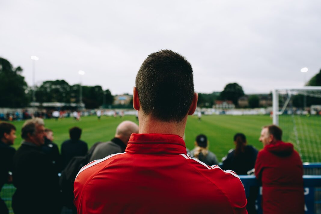 Photo by Richard Boyle man standing while watching soccer during daytime