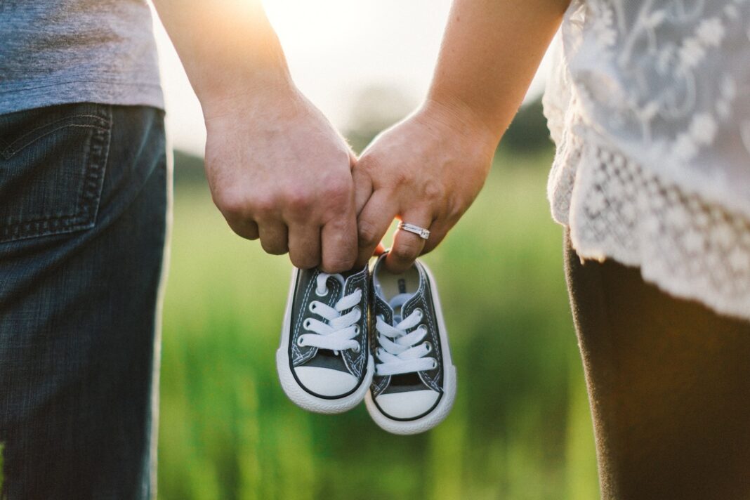 Photo by Drew Hays woman and man holding black crib shoes standing near green grass during daytime