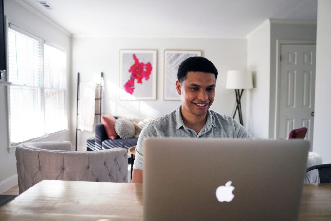 Photo by Joshua Mayo man in gray hoodie sitting on chair in front of silver macbook