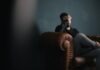 How You Can Use Online Gaming to Improve Your Mental Health (Without Letting it Take Over Your Life) a man holds his head while sitting on a sofa