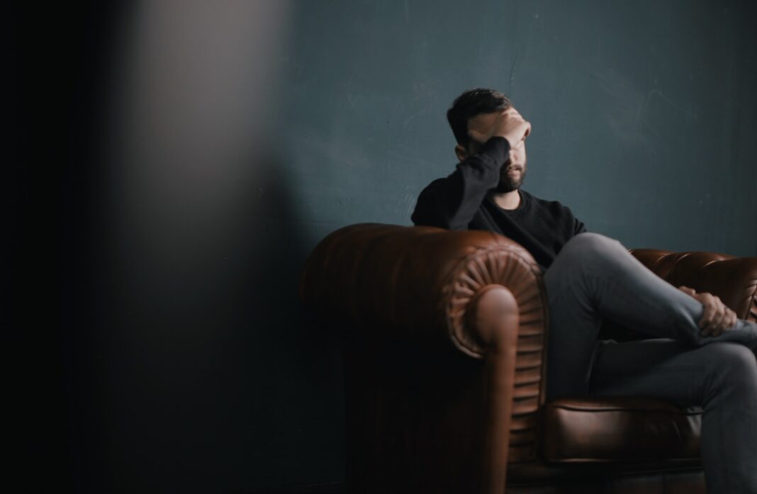 Photo by Nik Shuliahin 💛💙 a man holds his head while sitting on a sofa