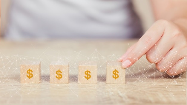 photo-woman-hand-arranging-wood-block-with-icon-mo Photo woman hand arranging wood block with icon money dollar growth finance and investment concept.