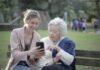 Caring for the Caregivers: Role of Health Insurance for Senior Citizens Delighted female relatives sitting together on wooden bench in park and browsing mobile phone while learning using
