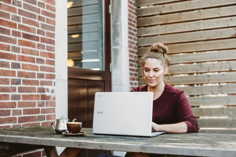 Photo by Anete Lūsiņa woman sitting and holding white Acer laptop near brown wooden wall