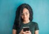 How To Bet Successfully in 2025: Tools and Tips for Smarter Betting Portrait of a smiling woman using her phone, wearing eyeglasses, against a vibrant blue background.