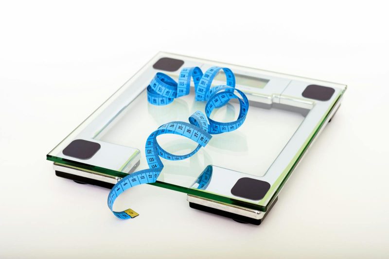 Photo by Pixabay A digital glass weighing scale with a blue measuring tape, symbolizing weight management.
