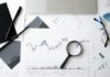 Top Resources Provided by the Best Stock Market Education Firms Flat lay of stock market analysis documents with magnifying glass, pens, and glasses.