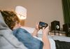 Security Trends in Mobile Gaming: Staying Safe in a Digital World Teen lying on sofa playing video games on smartphone indoors, surrounded by modern décor.