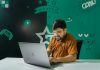 Register at Betongame Online to Explore Profitable Arbitrage Betting Opportunities A man with a beard and glasses smiles while gaming on a laptop indoors, decorated with gaming graphics.