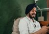A cheerful man in a turban using his smartphone while relaxing indoors.