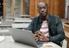 Passive Income Through Royalties: How It Works Stylish man with eyeglasses works on a laptop in an outdoor setting, relaxing with coffee.