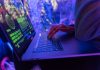 How Ransomware is Changing and What You Can Do to Protect Yourself Close-up of hands typing on a laptop displaying cybersecurity graphics, illuminated by purple light.