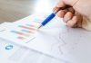 4 Ways Outdated Data Can Impair Business Efficiency A close-up of a hand with a pen analyzing data on colorful bar and line charts on paper.
