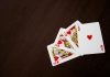 Why Travel the World When You Can Play From the Comfort of Your Own Home? Elegant flat lay of playing cards featuring ace of hearts on a wooden surface.