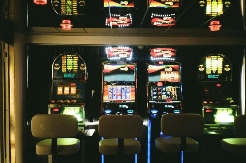 Photo by Darya Sannikova Slot machines in a dimly lit casino with reflective ceiling and empty chairs.
