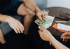 Factors to Consider Before Taking Out a Personal Loan Close-up of hands exchanging US dollar bills, symbolizing a financial transaction or payment.