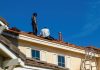 What You Need to Know About Roof Repair vs. Roof Replacement: Making the Right Call Roof construction scene with workers on a tiled roof, captured under a clear blue sky.