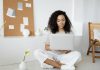 Top Productivity Tools Every Startup Founder Should Keep At Their Desk Young woman with curly hair working on her laptop in a cozy home setting, exuding confidence and focus.