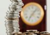 5 Proactive Financial Steps That Your Future Self Will Thank You For A close-up image of stacked coins with a blurred clock, symbolizing time and money relationship.
