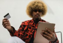 How to Protect Your Credit Card from Fraud and Scams Fashionable individual with afro hair using a tablet and credit card for online shopping indoors.
