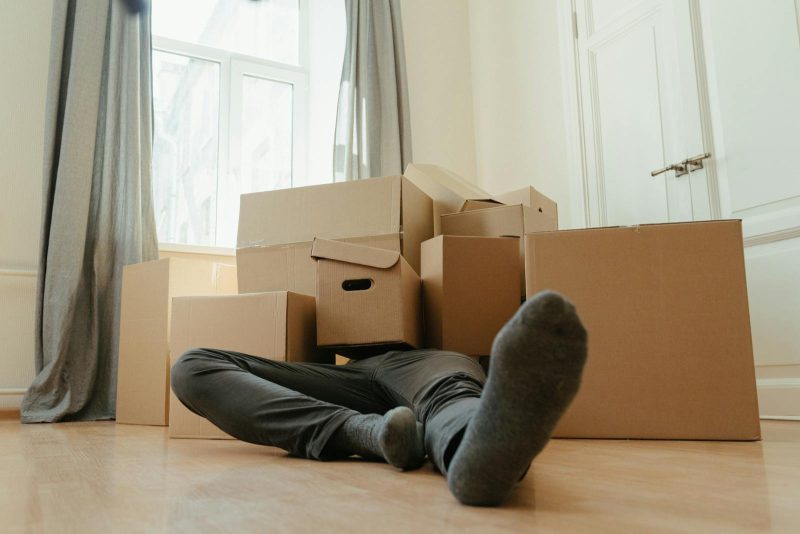 Photo by cottonbro studio A person lies down tired among cardboard boxes in a bright room, depicting moving day stress.