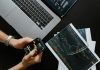 Can You Buy Fractional Shares on Thinkorswim? What Traders Should Know Hands using smartphone beside laptop with stock charts, showcasing digital trading.