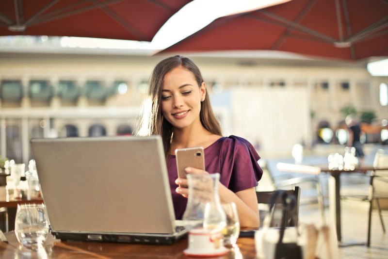 Photo by Andrea Piacquadio Woman enjoying remote work at a café, using a laptop and smartphone.