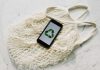 Overhead of smartphone with simple recycling sign on screen placed on white eco friendly mesh bag on marble table in room