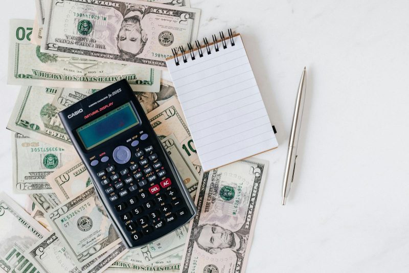Photo by Photo By: Kaboompics.com Flat lay of US dollar bills with calculator and notebook for budgeting.