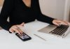 A professional woman multitasking with a smartphone and laptop at an office desk.