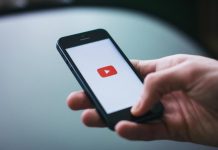 Best 5 YouTube Like Services That Don’t Use Bots Close-up of a hand holding a smartphone displaying the YouTube app on the screen.