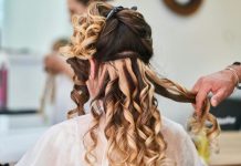 Workday Hair, The Kenna Kennor Way: Celebrity Advice for Everyday Professional Style From Britt Lower’s Husband Close-up of hairstylist perfecting curls on a woman's hair in a salon setting.