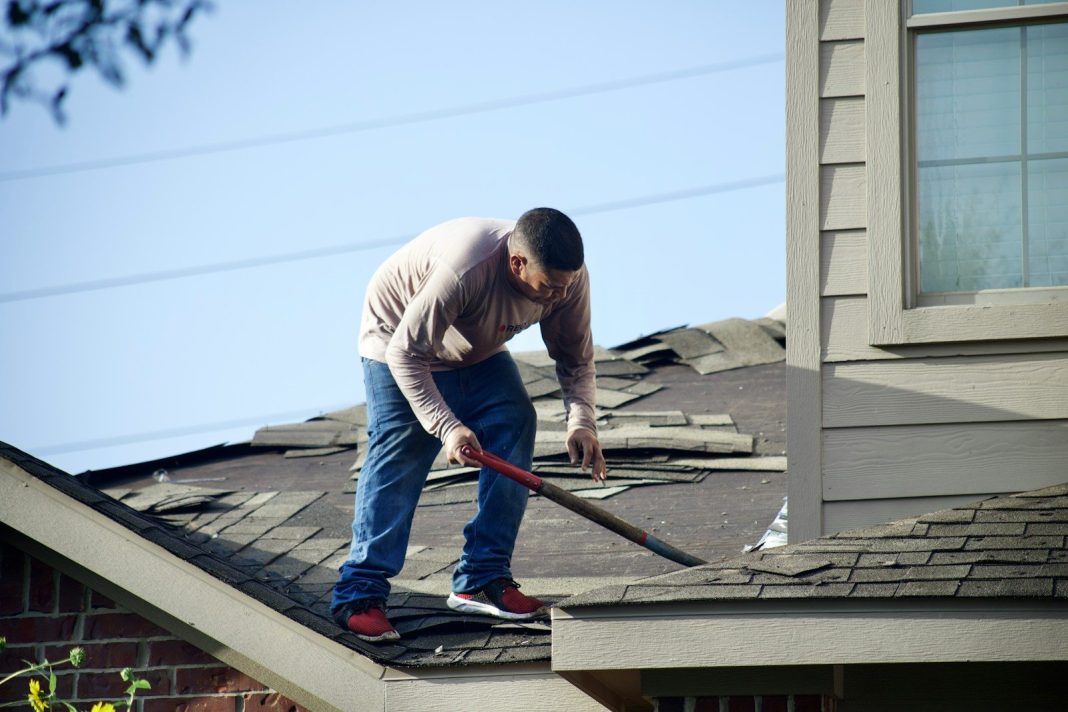 Photo by Zohair Mirza a man with a hammer on top of a roof
