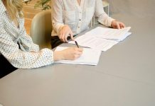 5 Essential Documents Everyone Needs in an Estate Plan woman signing on white printer paper beside woman about to touch the documents