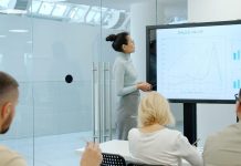6 Business Processes That Benefit From Better Reporting Tools Woman presents charts on a screen to colleagues.