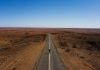 gray concrete road between brown field under blue sky during daytime