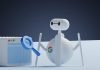 a white robot holding a magnifying glass next to a white box
