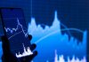a person holding a cell phone in front of a stock chart