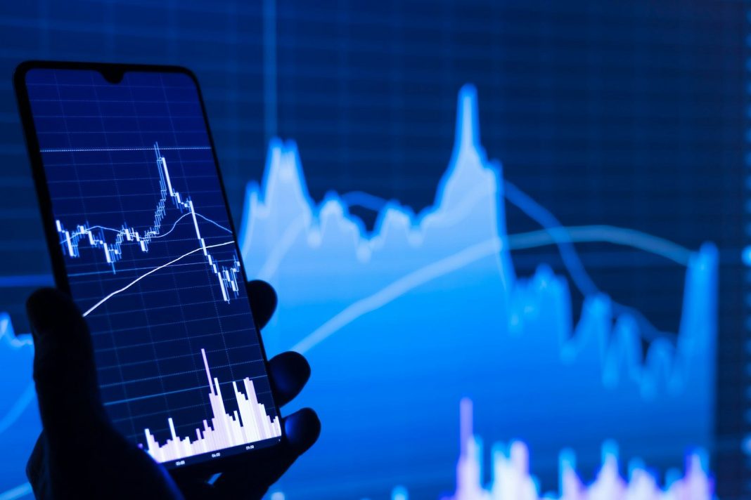 Photo by Adam Åšmigielski a person holding a cell phone in front of a stock chart