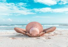 How to Plan a Restorative Vacation That Actually Combats Burnout woman in brown sun hat lying on sand during daytime