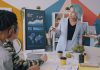 A woman with blue hair presenting data on a monitor to a team