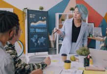 Why Top Executives Are Moving Strategic Off-Sites to Global Business Hubs A woman with blue hair presenting data on a monitor to a team